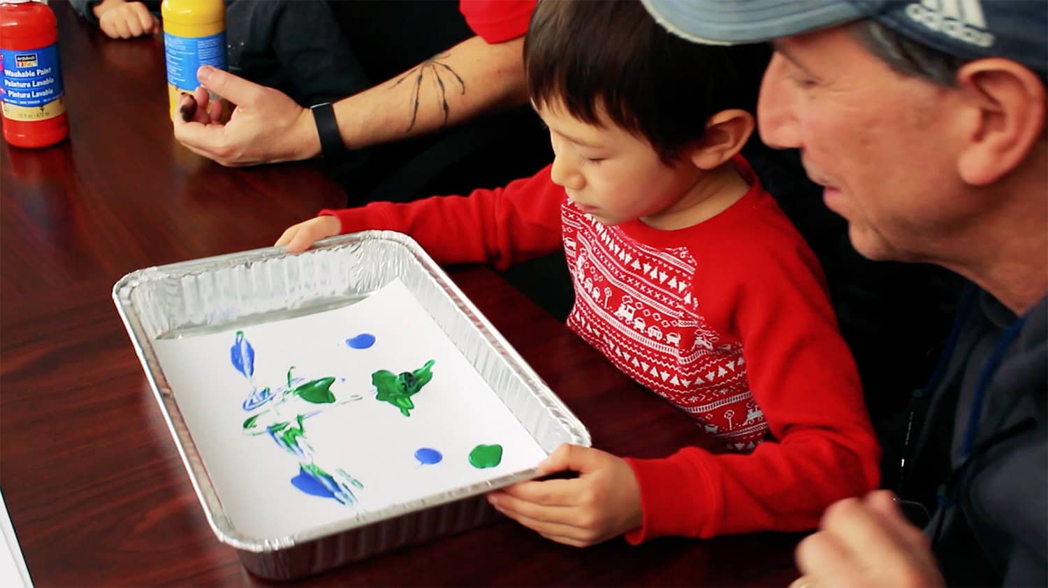 Young child and adult observing colorful paint on a tray during a science activity.