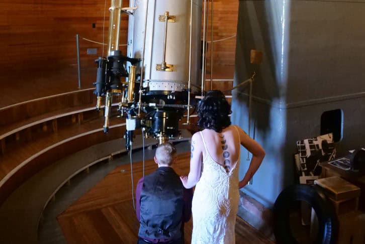 Two people observing a large telescope at Lowell Observatory, one in a white dress and the other in.
