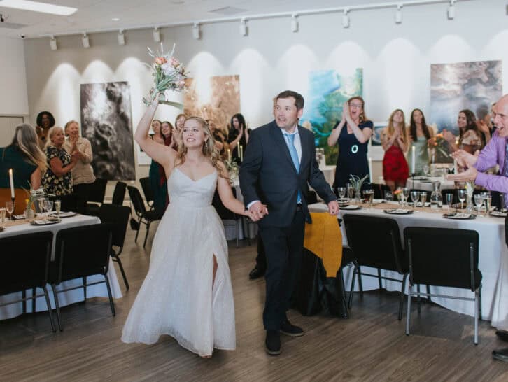 Bride and groom dancing at wedding reception with guests in art gallery setting.