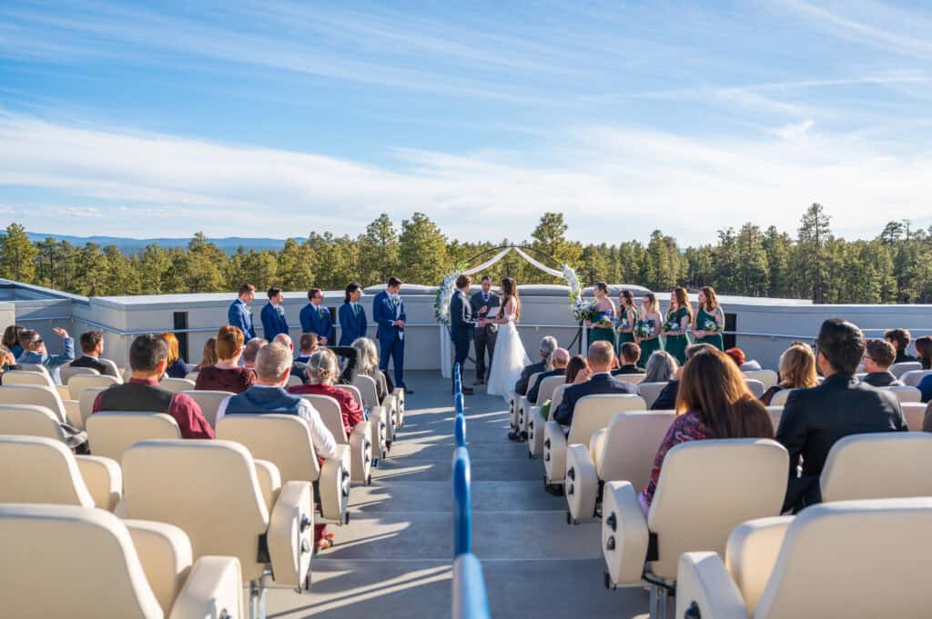 Wedding ceremony on rooftop with guests, bride, groom, and wedding party, city skyline in background.