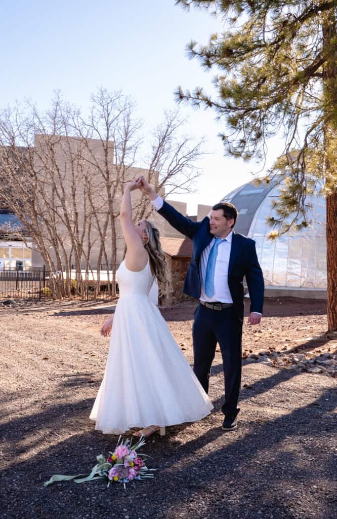 Bride and groom dancing outdoors at Lowell Observatory with trees and observatory building in the背景.
