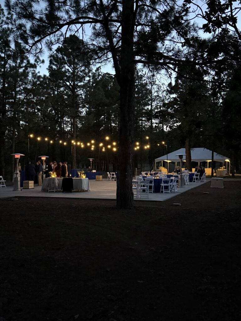 Outdoor evening event at Lowell Observatory with string lights and tables under trees.